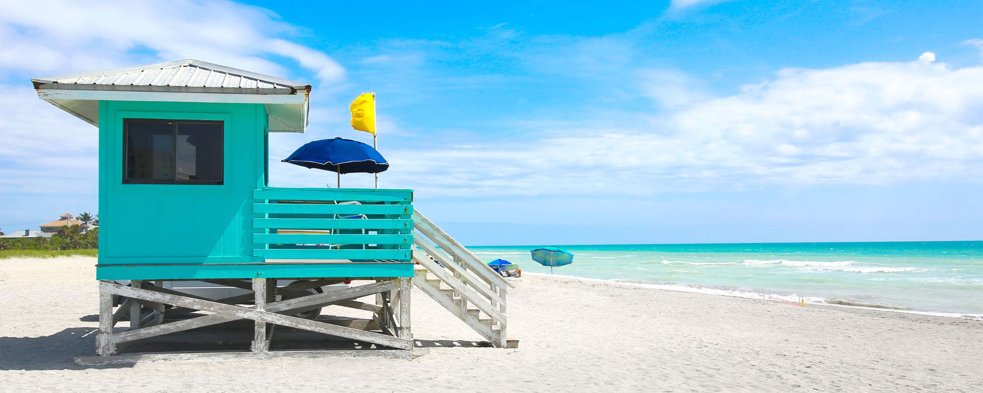 Colorful lifeguard station on a sandy beach with umbrellas and a clear blue sky in Venice.